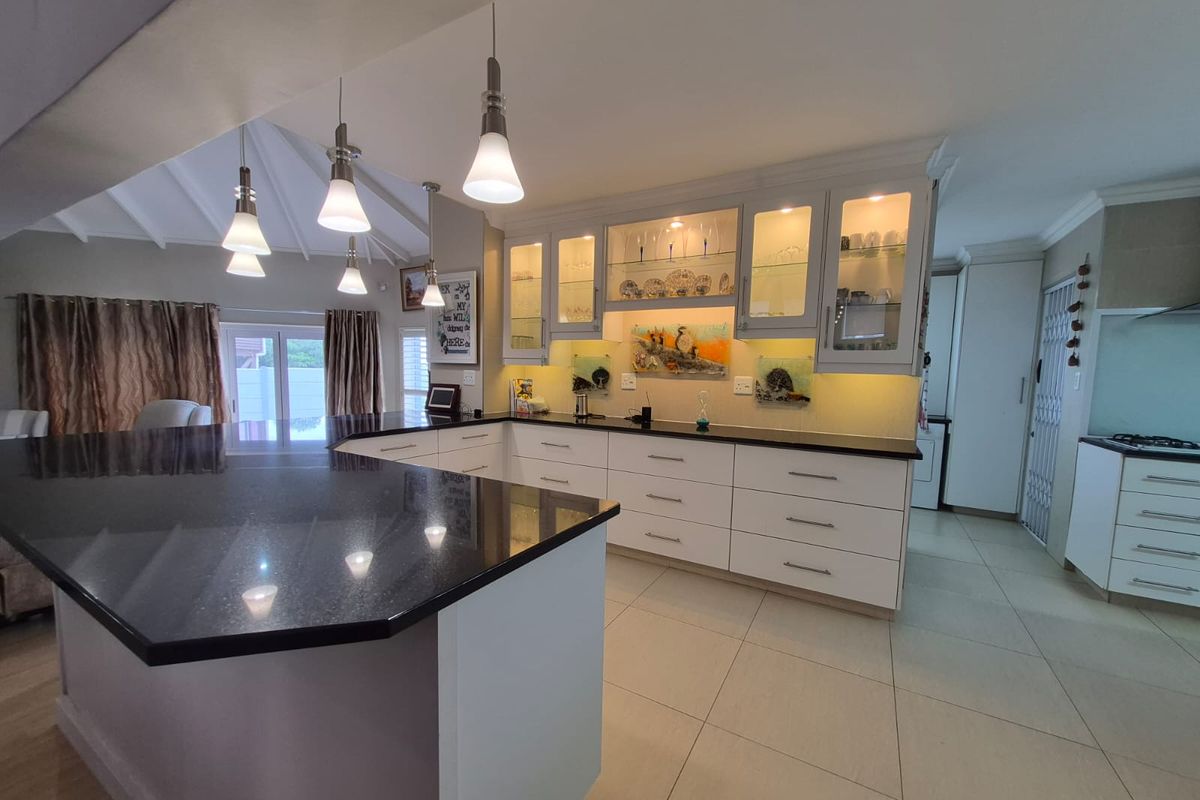 Modern kitchen featuring white cabinetry, black granite countertops, a central island, and integrated under-cabinet lighting, creating a bright and functional culinary space.