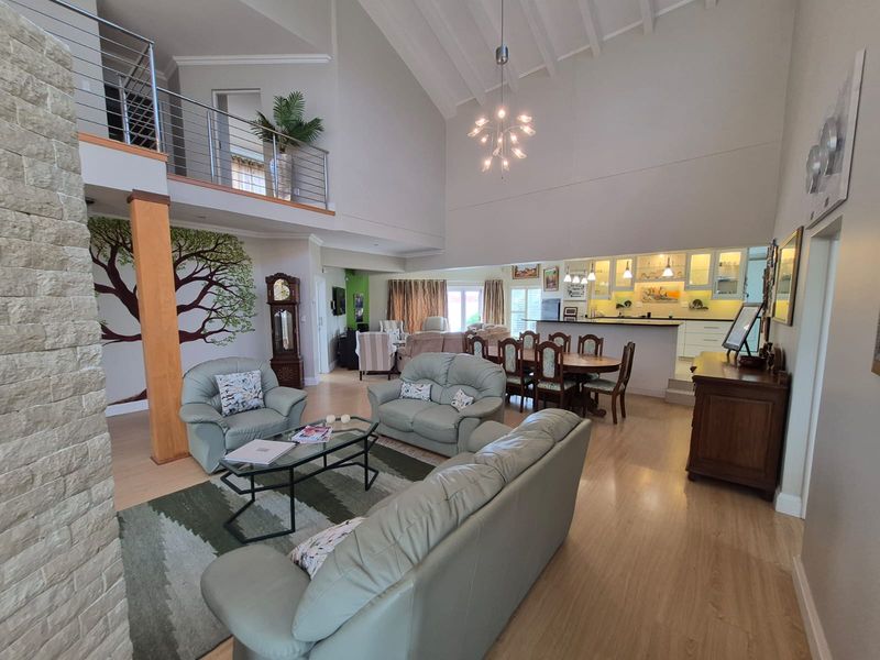 Spacious open-plan living and dining area featuring a double-volume vaulted ceiling, mezzanine level, stone feature wall, and a well-appointed kitchen with island.