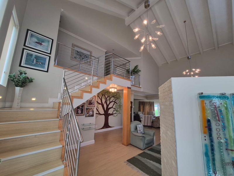 Spacious living area featuring a striking staircase with stainless steel balustrades, vaulted ceilings with exposed beams, and a modern stone feature wall.