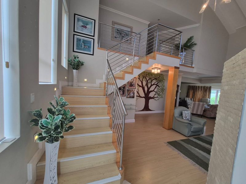 Spacious entrance hall featuring a modern staircase with stainless steel balustrades, laminate flooring, and high vaulted ceilings leading into an open-plan living area.