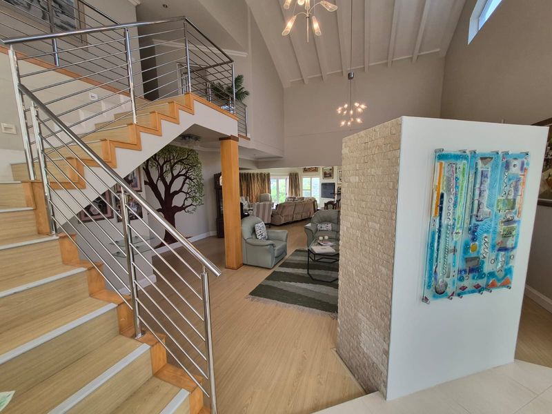 Spacious open-plan living area featuring a striking timber staircase with stainless steel railings, vaulted ceilings, and a decorative stone feature wall.