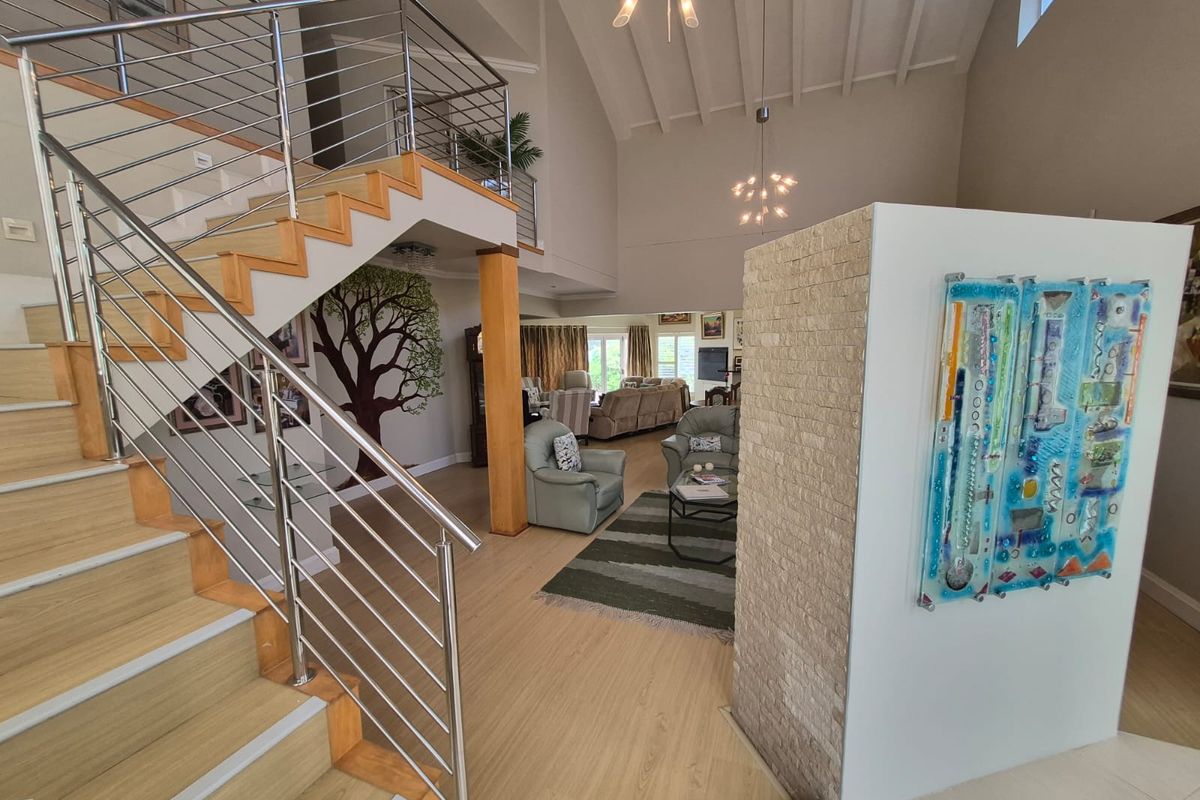 Spacious open-plan living area featuring a striking timber staircase with stainless steel railings, vaulted ceilings, and a decorative stone feature wall.
