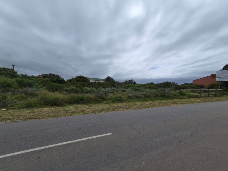 A vacant residential plot of land featuring natural vegetation, a timber fence, and direct access from a paved street.