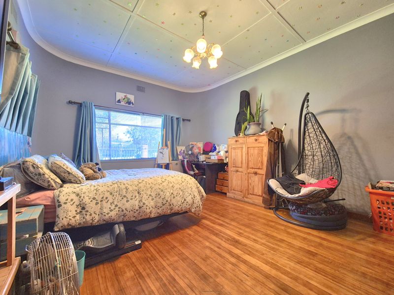 A spacious bedroom featuring original hardwood flooring, coved ceilings with decorative detailing, and a central light fixture.