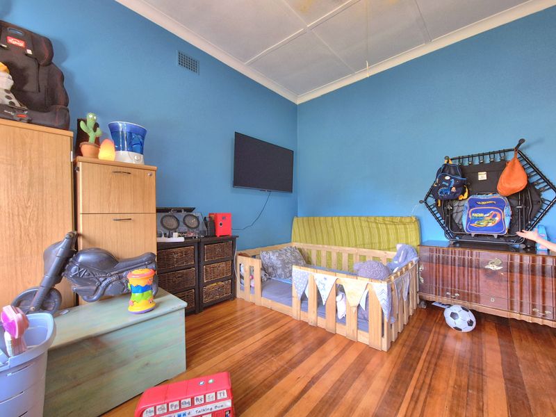 A bedroom featuring polished hardwood flooring and a wall-mounted television, showing visible signs of water staining on the ceiling tiles.