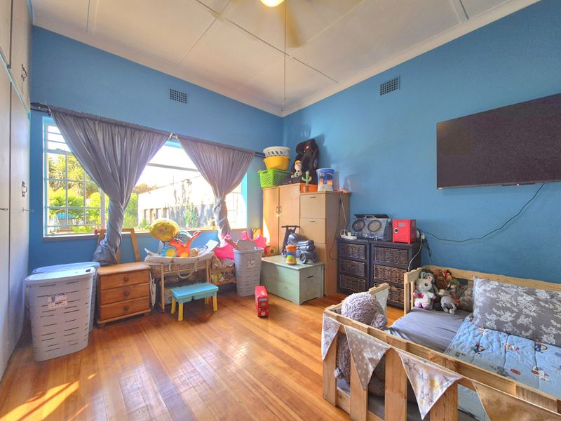A bedroom featuring polished hardwood flooring, built-in storage cupboards, and a ceiling fan, finished with blue wall paint.