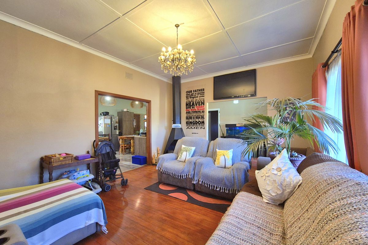 A living room featuring hardwood flooring, a suspended fireplace, and a chandelier, with an open-plan flow leading into the adjacent kitchen area.
