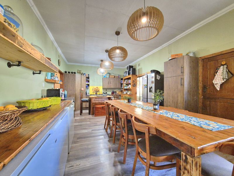 Spacious open-plan kitchen and dining area featuring rustic wooden cabinetry, laminate flooring, and multiple pendant lights, offering a warm and functional living space.