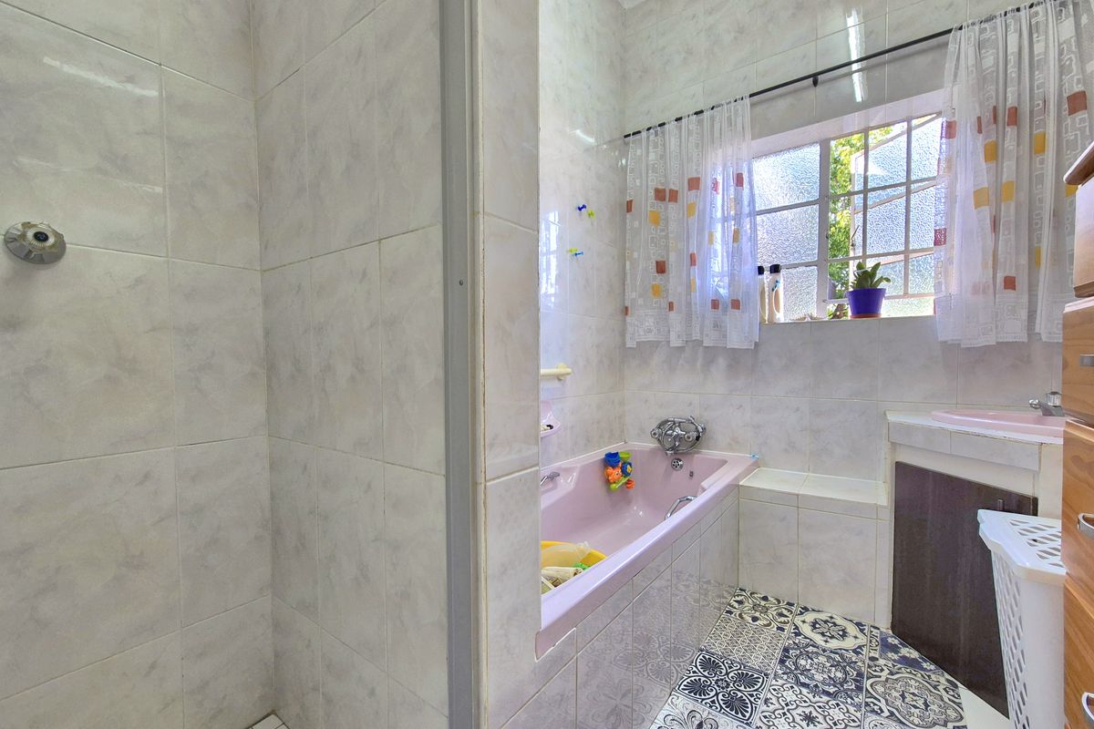 A functional bathroom featuring a built-in bathtub, separate shower enclosure, and a vanity unit, finished with tiled walls and decorative patterned floor tiles.