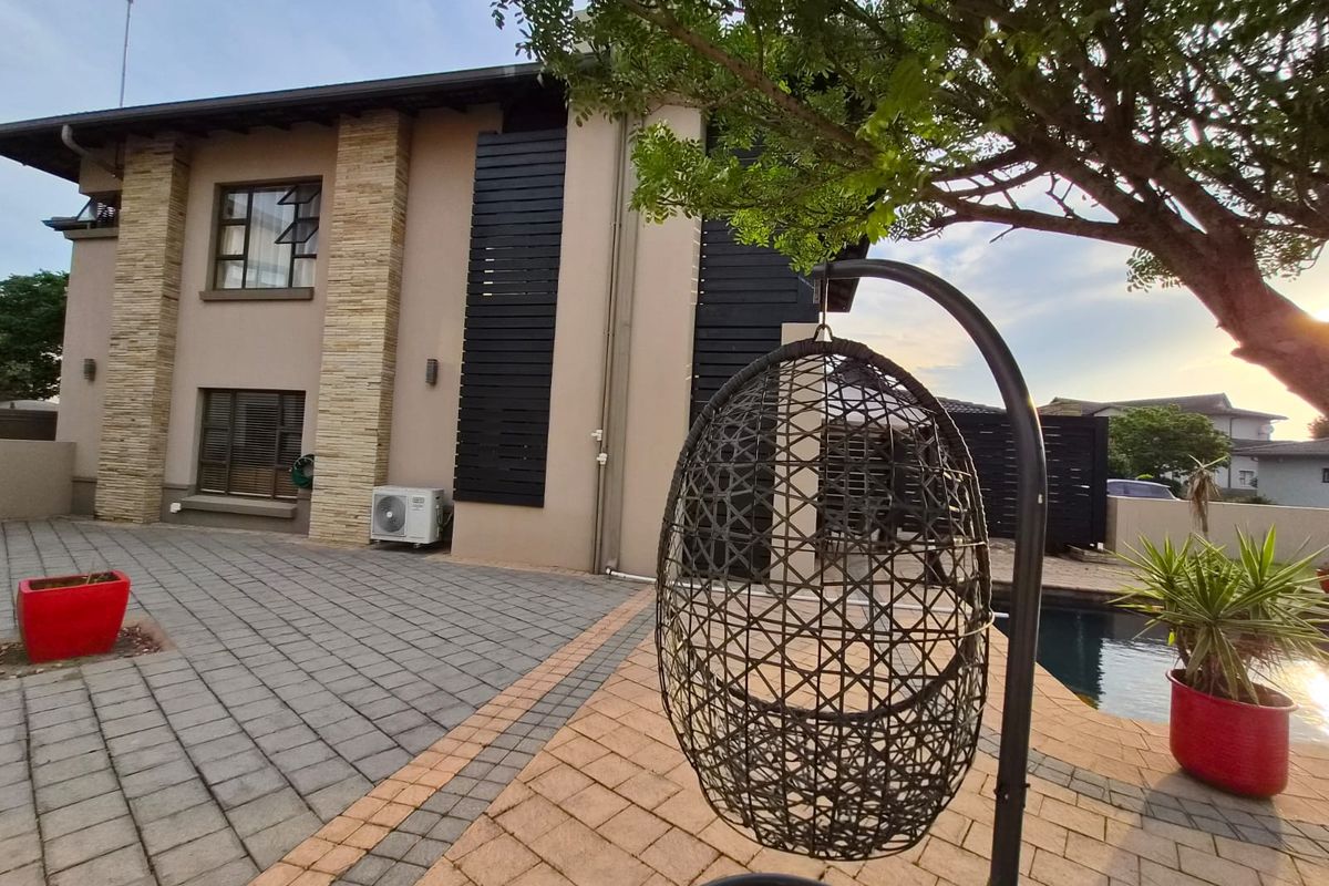 Rear exterior view featuring a paved patio area, swimming pool, and modern architectural details including stone cladding and timber privacy screens.