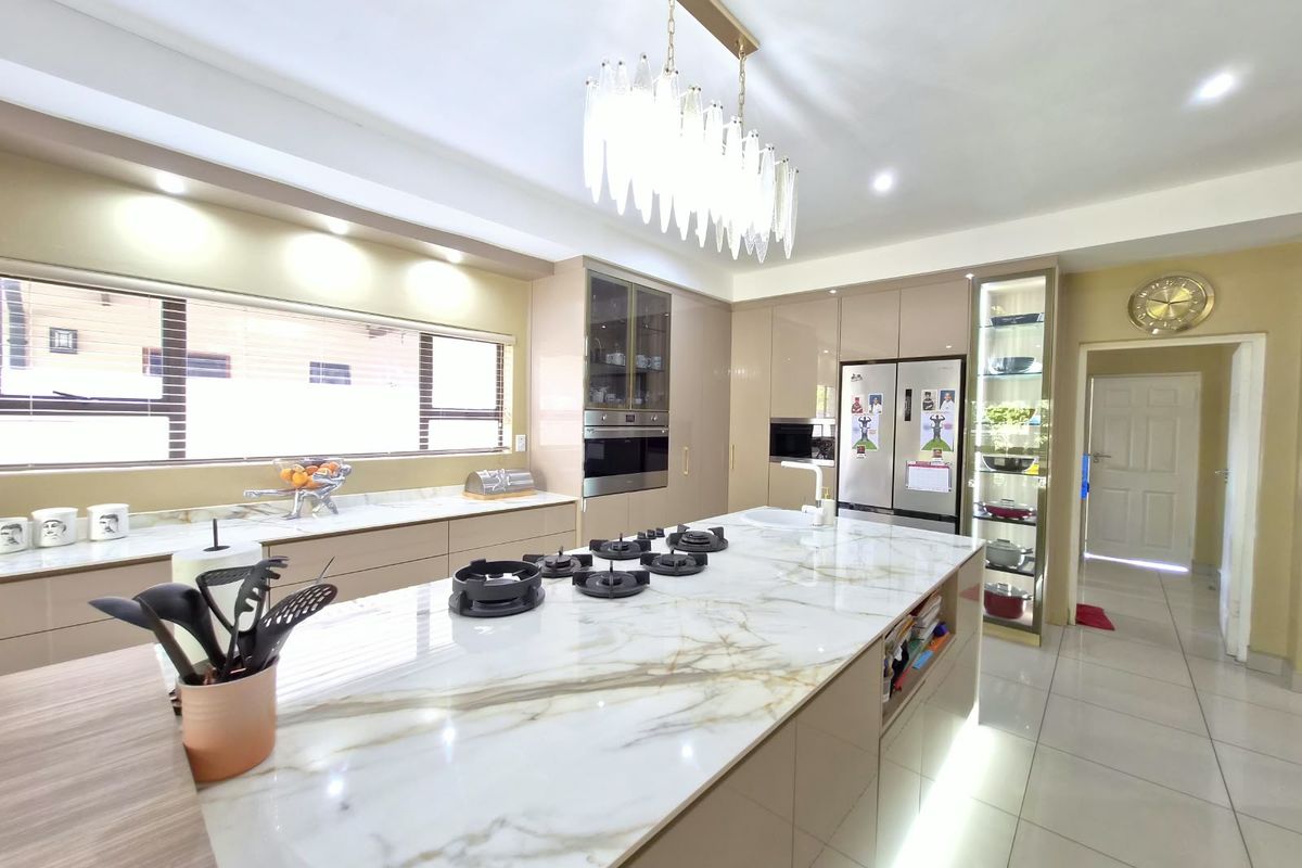Modern kitchen featuring a large marble-topped island with a gas hob, integrated cabinetry, built-in appliances, and elegant pendant lighting.