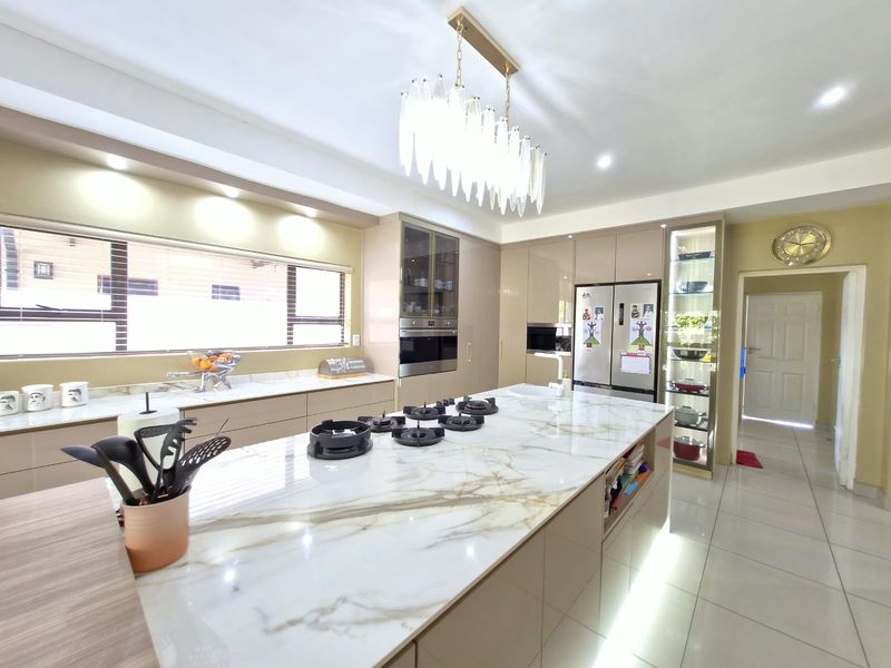 Modern kitchen featuring a large marble-topped island with a gas hob, integrated cabinetry, built-in appliances, and elegant pendant lighting.