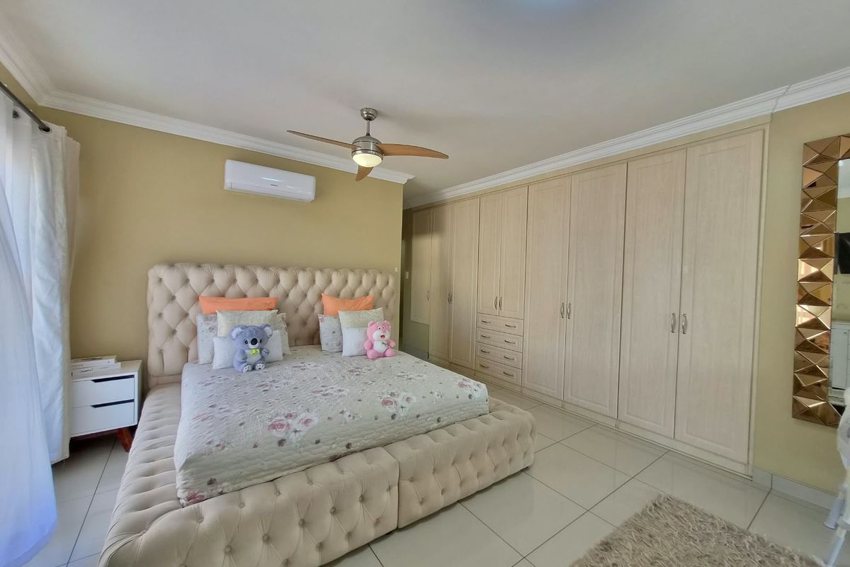 Spacious bedroom featuring extensive built-in cupboards, tiled flooring, a ceiling fan, and a wall-mounted air conditioning unit.