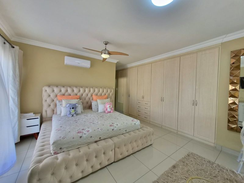 Spacious bedroom featuring extensive built-in cupboards, tiled flooring, a ceiling fan, and a wall-mounted air conditioning unit.