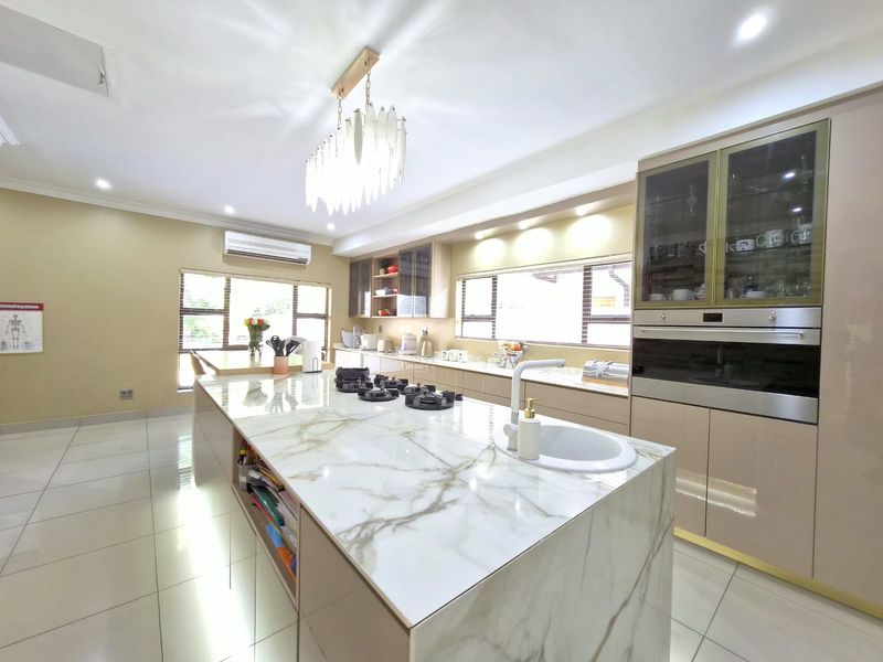 Modern kitchen featuring a large marble-look island with integrated gas hob and sink, high-gloss cabinetry, built-in oven, and elegant pendant lighting.