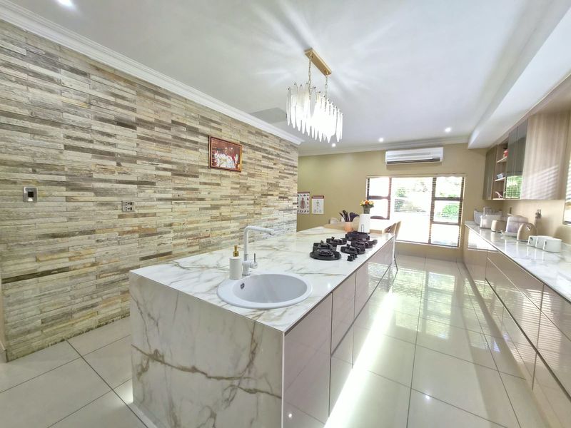 Modern kitchen featuring a large marble-look island with integrated gas hob and sink, complemented by a striking stone-clad feature wall and sleek cabinetry.