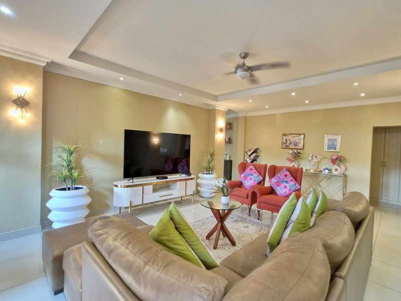 Spacious living room featuring a recessed ceiling with downlights, a ceiling fan, wall sconces, and neutral tiled flooring.