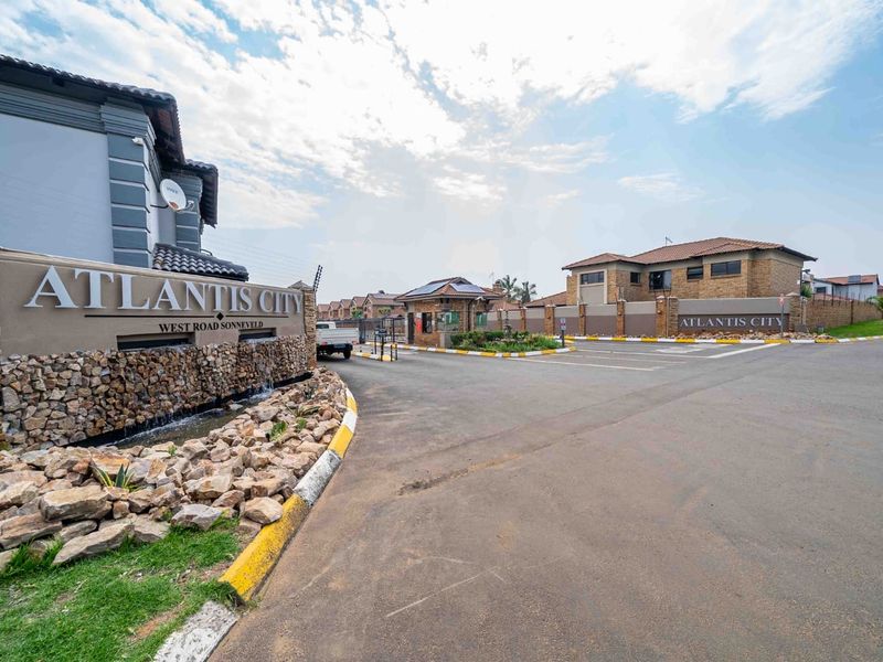 Entrance view of Atlantis City townhouse complex featuring stone-clad signage, a water feature, and secure gated access with perimeter fencing.