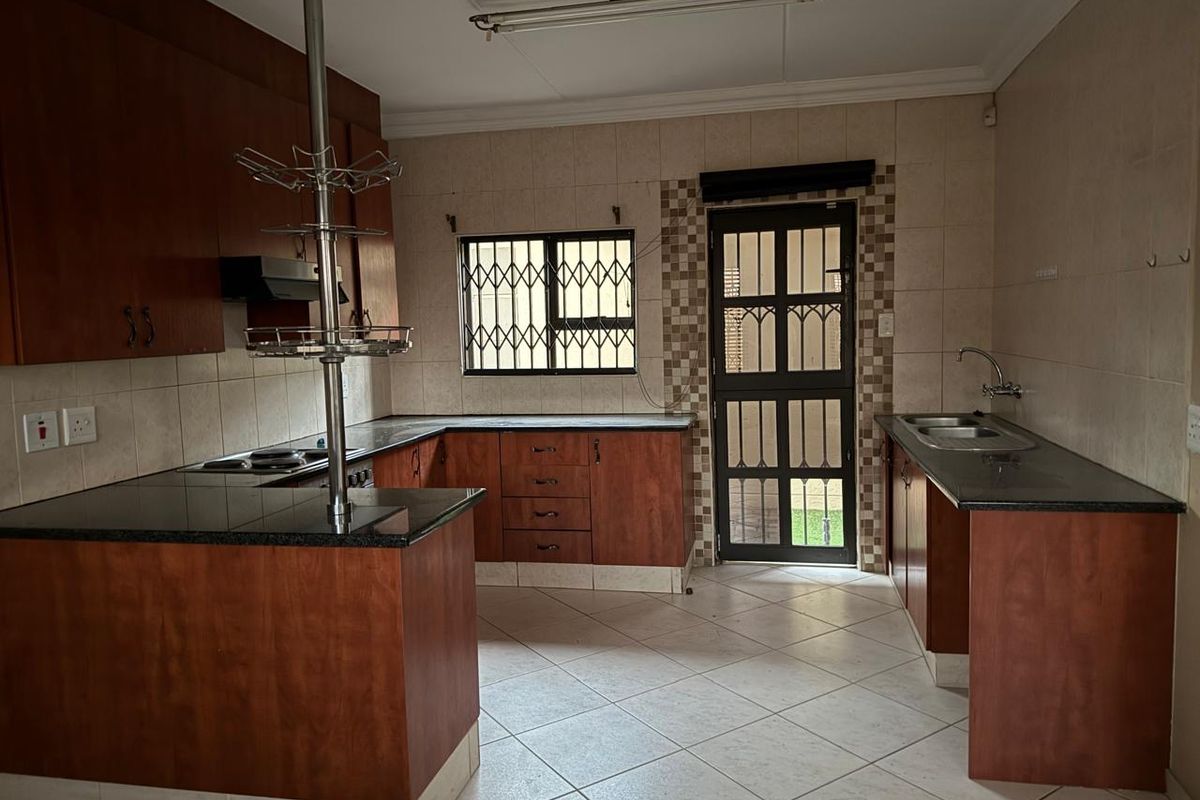 A functional kitchen featuring wooden cabinetry, granite countertops, a double bowl sink, and a built-in hob, with direct access to the exterior.