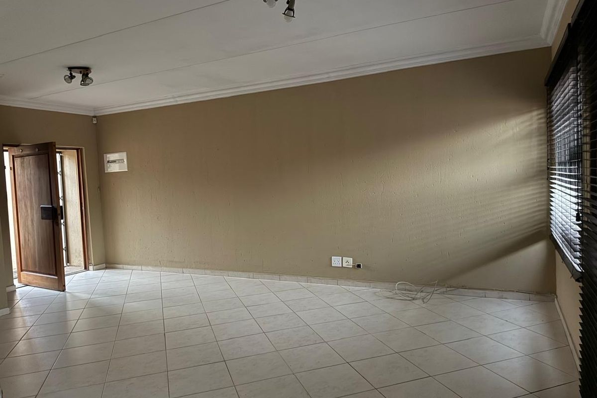 An empty living room featuring tiled flooring, neutral wall tones, and natural light filtered through venetian blinds, offering a blank canvas for interior design.