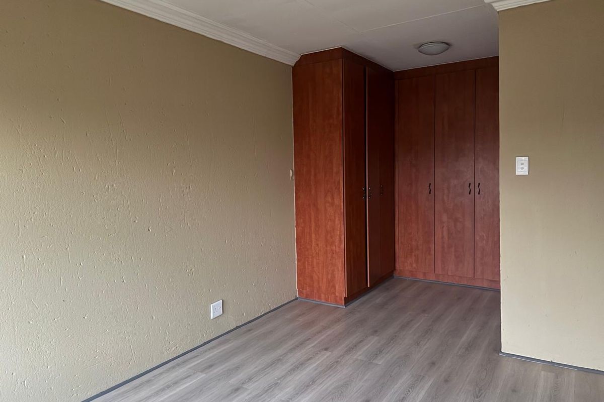 An empty bedroom featuring laminate flooring, built-in wooden cupboards, and neutral wall finishes with ceiling cornice detailing.