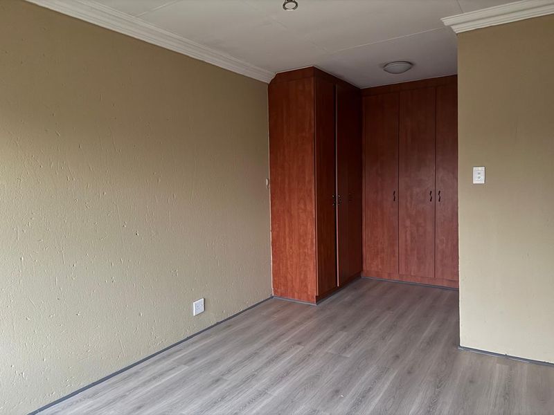 An empty bedroom featuring laminate flooring, built-in wooden cupboards, and neutral wall finishes with ceiling cornice detailing.