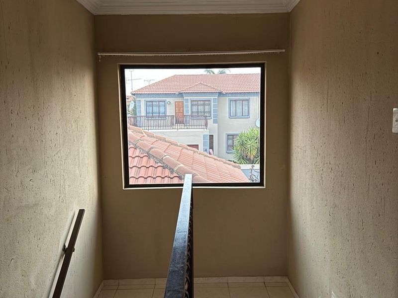 A bright staircase landing area featuring tiled flooring, a metal balustrade, and a large window providing natural light and views of the surrounding complex.