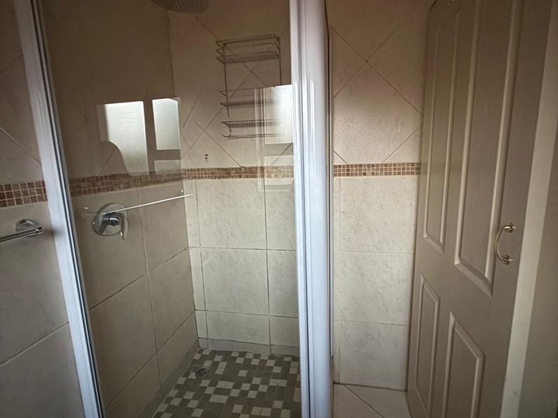 A functional bathroom featuring a glass-enclosed shower with tiled walls and flooring, presenting a clean and neutral aesthetic.