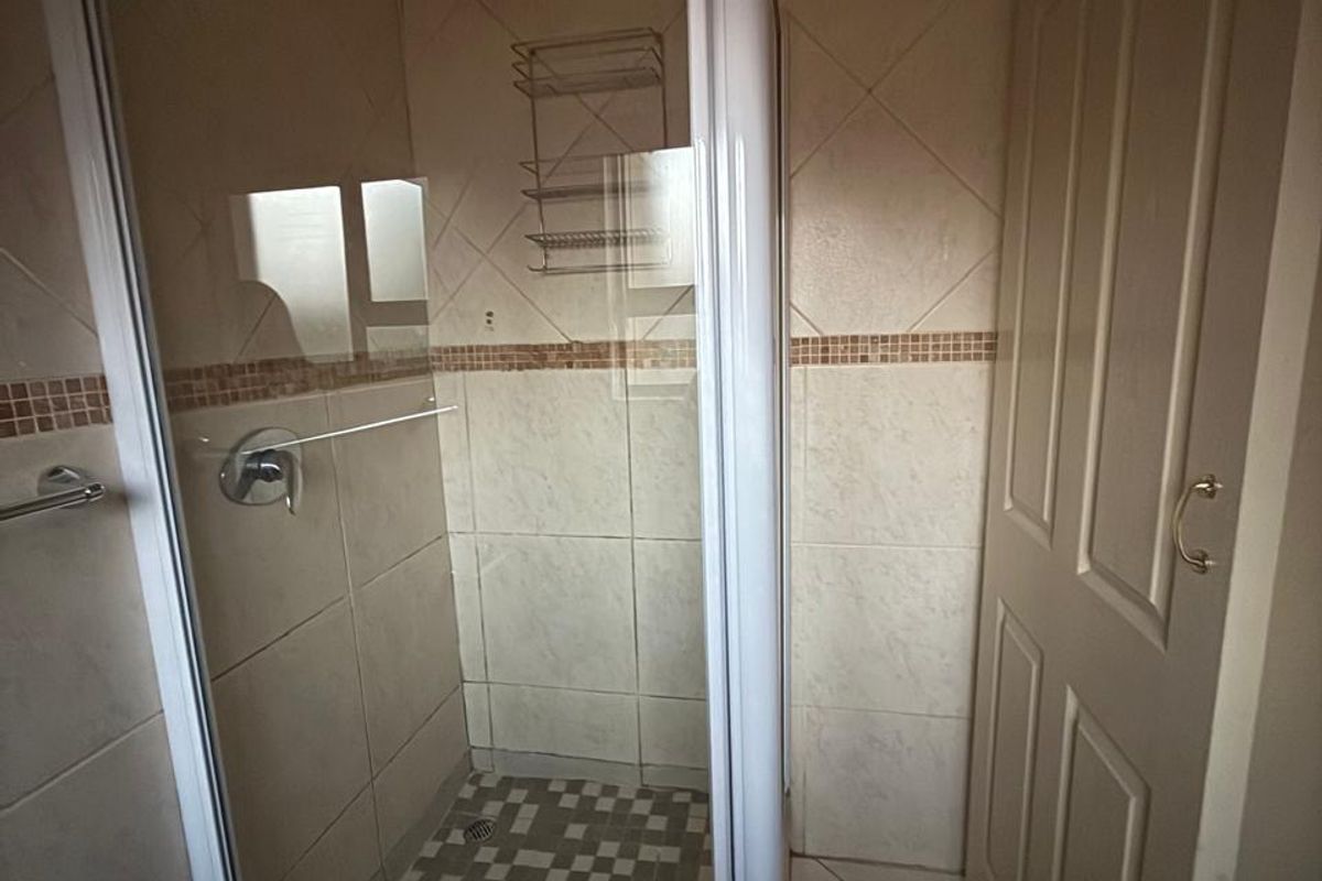 A functional bathroom featuring a glass-enclosed shower with tiled walls and flooring, presenting a clean and neutral aesthetic.