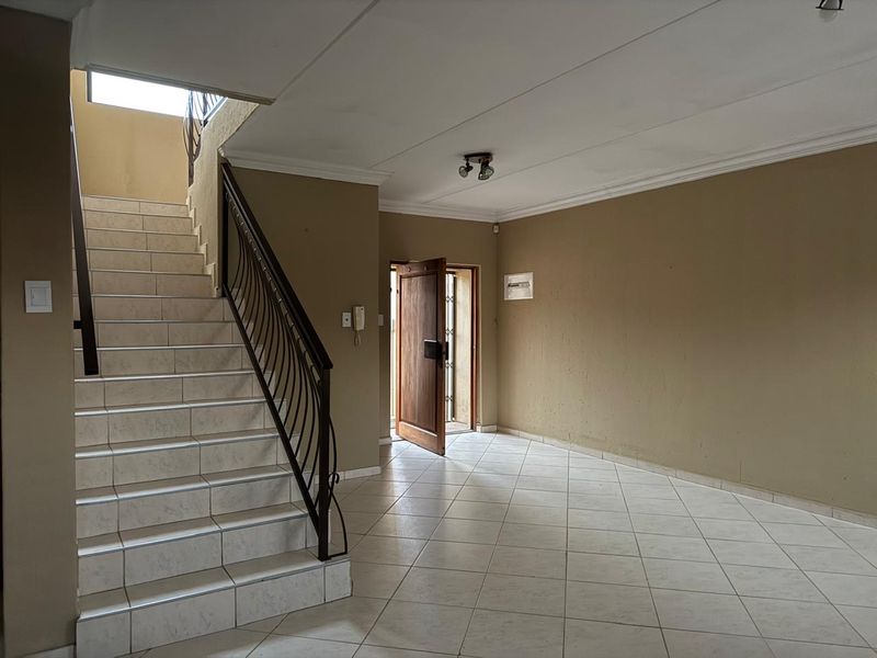 Spacious entrance hall featuring tiled flooring, a staircase with a wrought iron balustrade, and direct access to the front door.