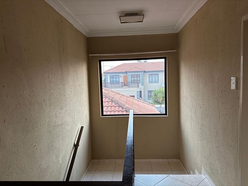 A functional staircase landing area featuring tiled flooring, a handrail, and a window providing natural light and a view of the surrounding neighborhood.