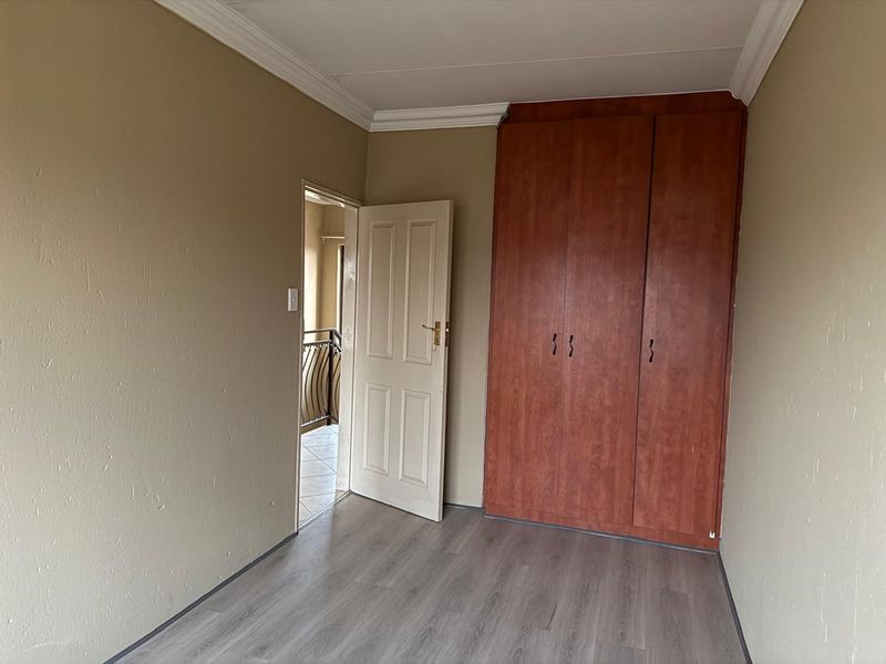 An empty bedroom featuring laminate flooring, neutral wall paint, and a built-in wooden wardrobe.
