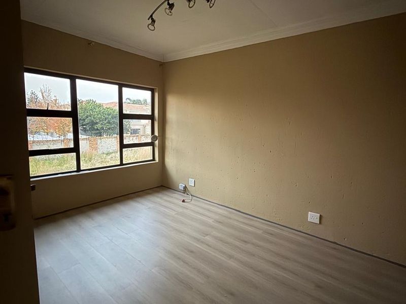An empty bedroom featuring laminate flooring, a large window, and a ceiling-mounted spotlight fixture, ready for personalization.