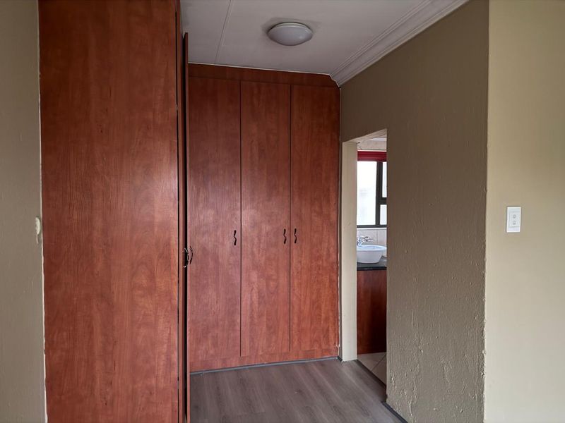 A bedroom featuring built-in wooden cupboards, laminate flooring, and a view into an adjacent bathroom area.