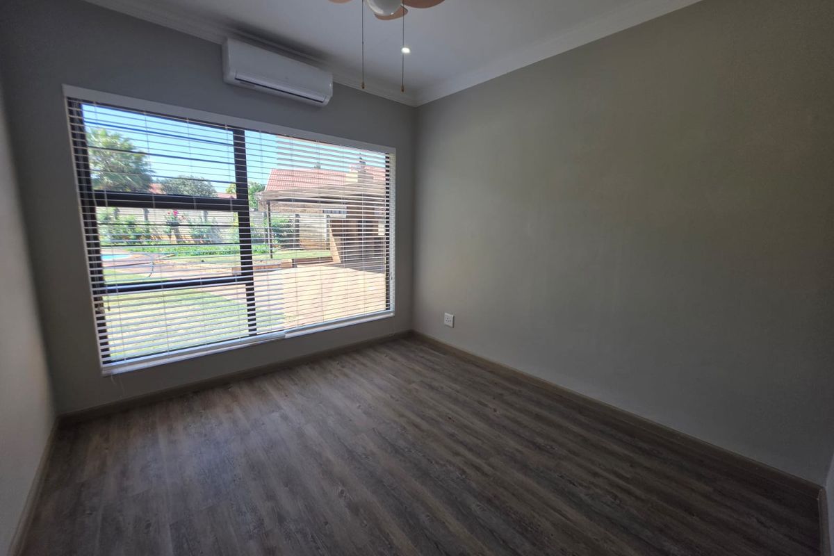 A bright, empty bedroom featuring modern laminate flooring, a ceiling fan, and a wall-mounted split-system air conditioner with views of the garden.