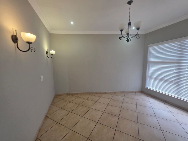 A bright, empty living area featuring neutral walls, tiled flooring, decorative wall sconces, a central chandelier, and venetian blinds.