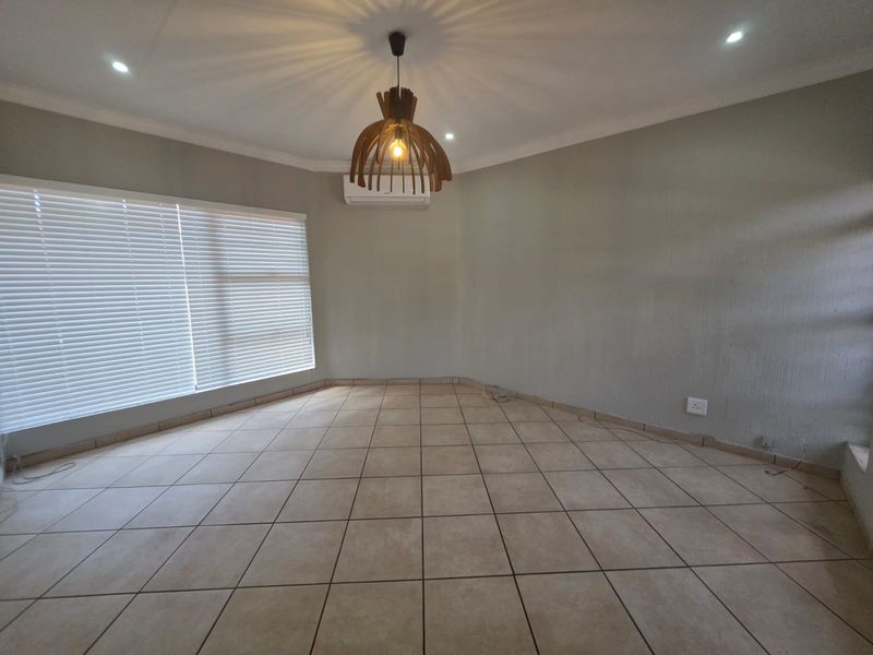 A spacious, empty living area featuring neutral tiled flooring, an installed air conditioning unit, and modern venetian blinds, ready for personalization.