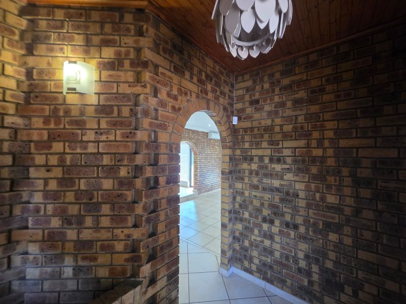 A spacious hallway featuring rustic exposed brick walls, a classic arched entryway, and tiled flooring, leading into an adjacent living area.