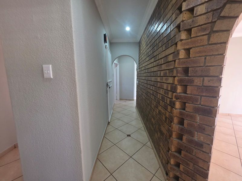 A bright hallway featuring a textured exposed brick wall, ceramic floor tiles, and an arched transition leading to other areas of the home.
