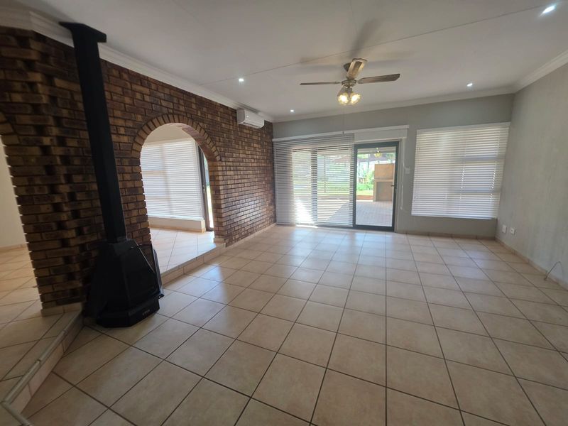 Spacious living area featuring tiled flooring, a brick fireplace, ceiling fan, air conditioning, and large sliding doors leading to the outdoor patio.