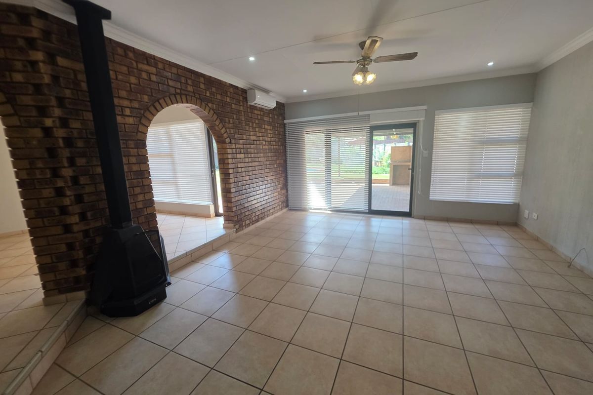 Spacious living area featuring tiled flooring, a brick fireplace, ceiling fan, air conditioning, and large sliding doors leading to the outdoor patio.