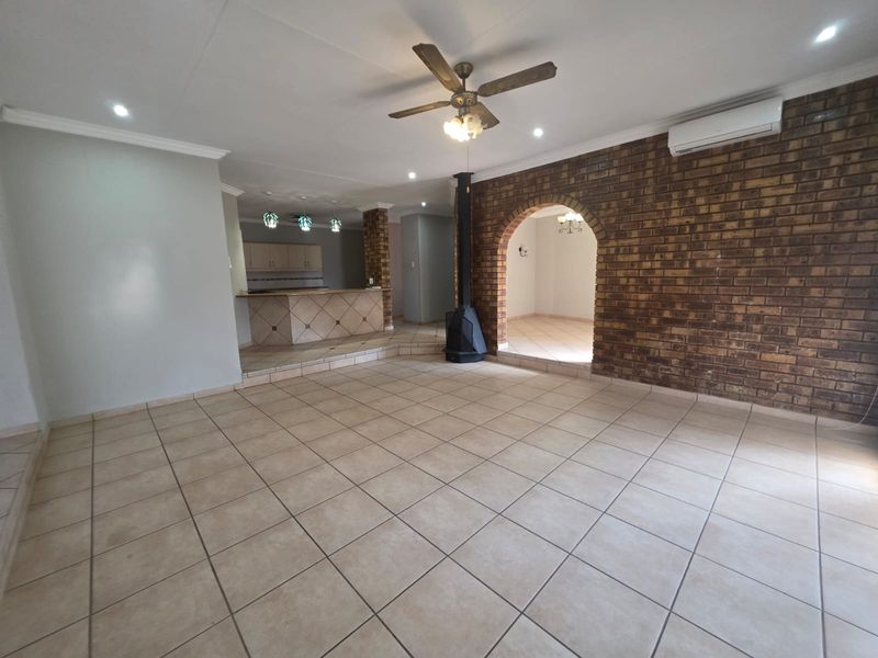 Spacious open-plan living area featuring tiled floors, an exposed brick feature wall with an archway, a freestanding fireplace, and integrated kitchen cabinetry.