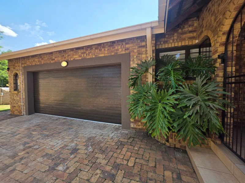Front exterior view featuring a brick facade, a modern sectional garage door, and a paved driveway with established landscaping.