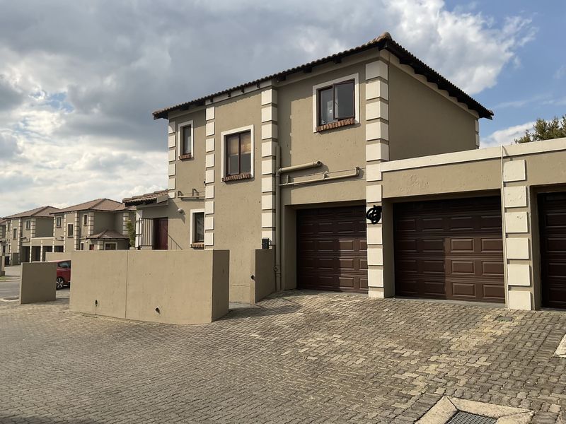 Front exterior view of a double-story townhouse featuring a double garage, paved driveway, and plastered facade with decorative corner detailing.