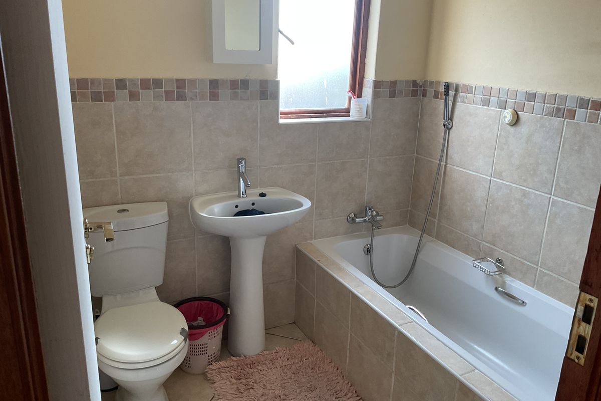 A functional bathroom featuring a pedestal basin, toilet, and a bathtub with a handheld shower mixer, finished with neutral wall tiling.