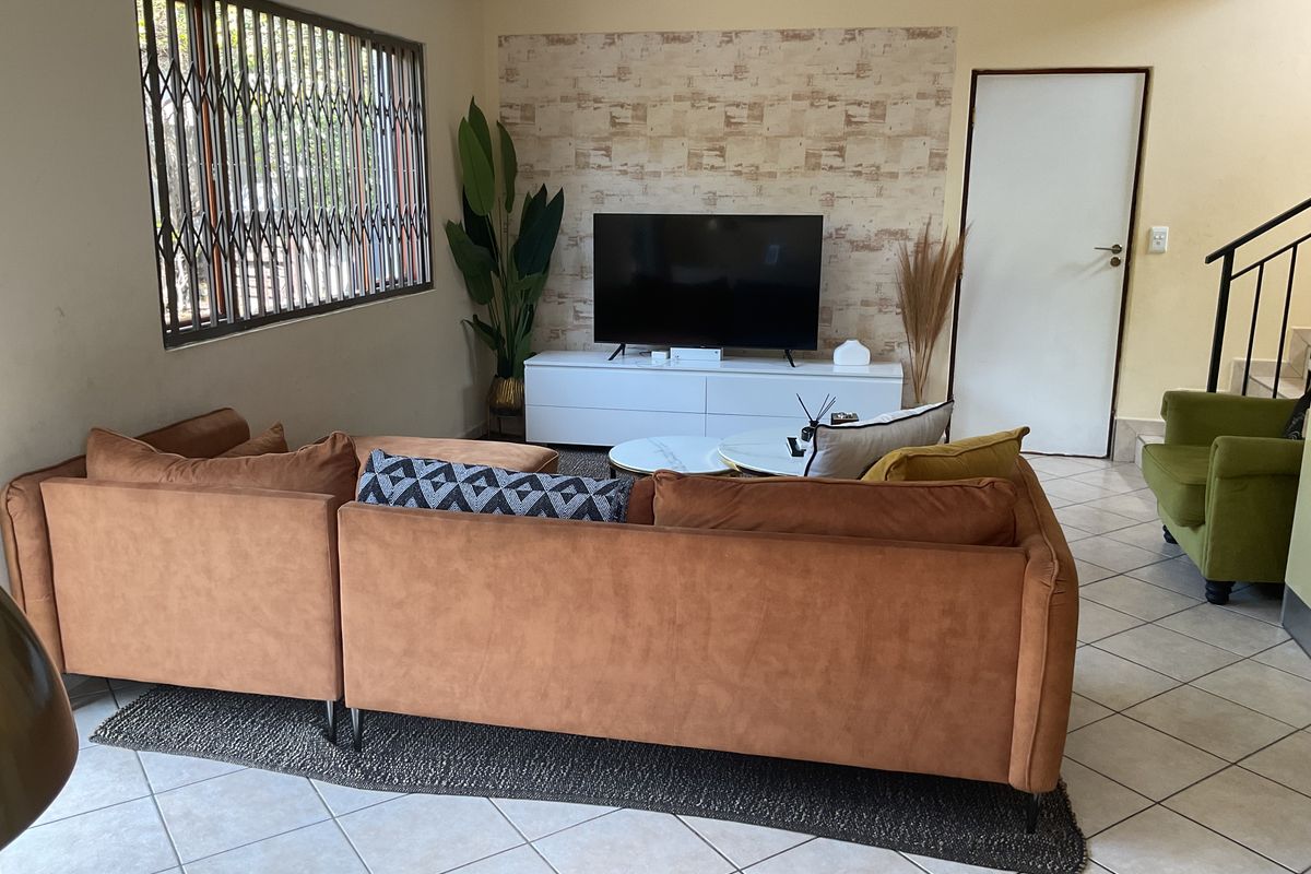 A comfortable living room featuring tiled flooring, a decorative feature wall, and a window fitted with a security gate.
