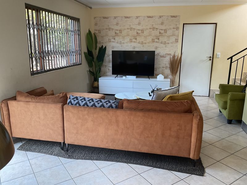 A comfortable living room featuring tiled flooring, a decorative feature wall, and a window fitted with a security gate.