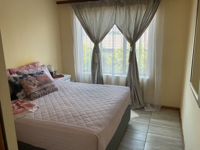 A cozy bedroom featuring tiled flooring and a large window with curtain treatments, providing natural light and a view of the exterior.