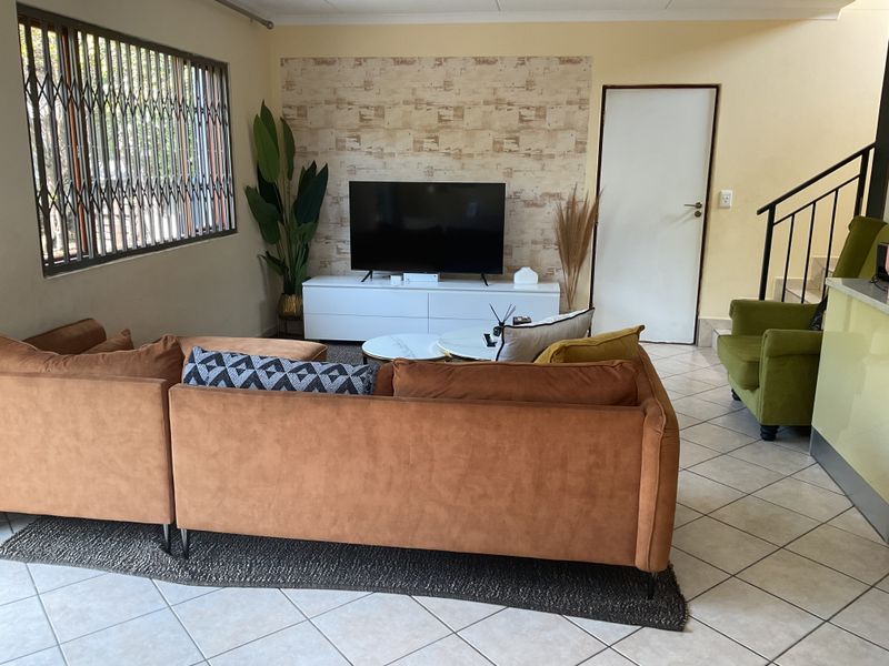 A living room featuring tiled flooring, a staircase, and a decorative feature wall with a security gate on the window.