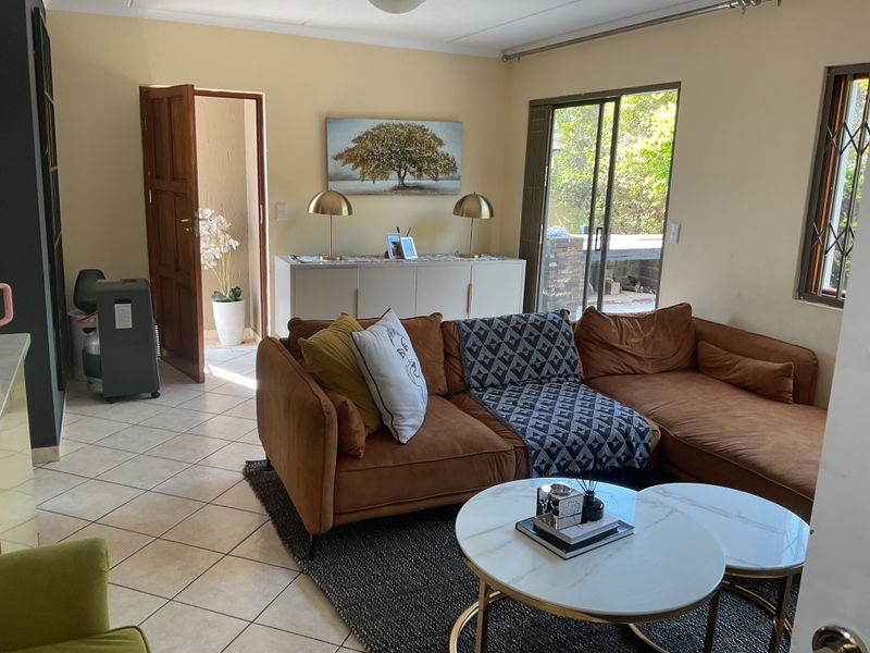 A comfortable living room featuring tiled flooring, a sliding glass door leading to the patio, and a security gate on the window.